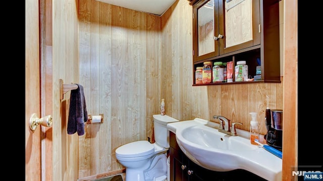 half bath with toilet, wood walls, and vanity