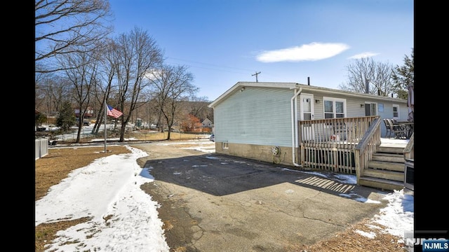 snow covered property with aphalt driveway and a wooden deck