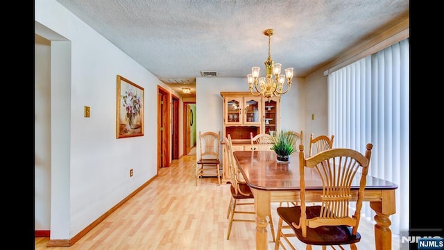 dining room featuring a notable chandelier, visible vents, light wood-style flooring, a textured ceiling, and baseboards