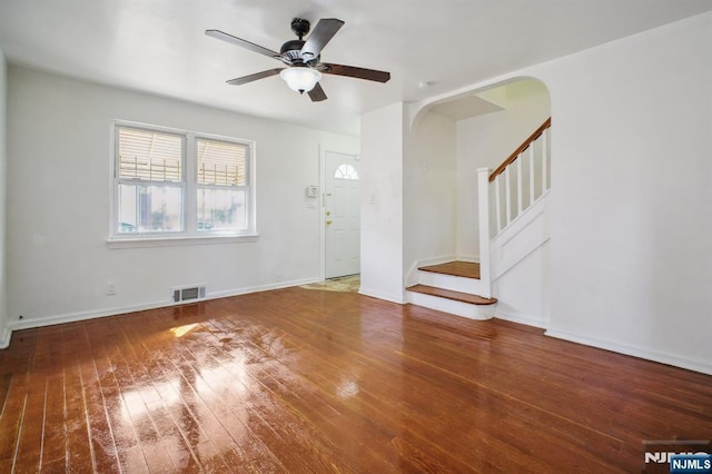 unfurnished living room featuring arched walkways, visible vents, wood finished floors, baseboards, and stairs