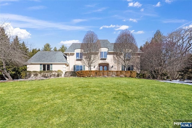 french country style house with a front lawn, roof with shingles, and stucco siding