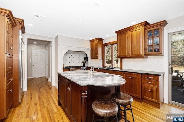 kitchen featuring visible vents, glass insert cabinets, a sink, dark stone countertops, and an island with sink