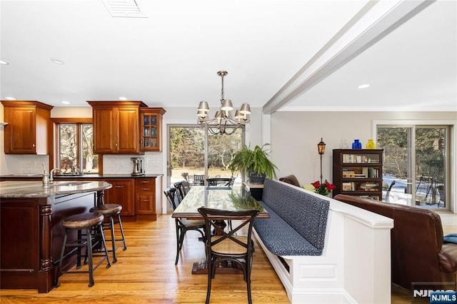 kitchen featuring pendant lighting, light wood finished floors, visible vents, glass insert cabinets, and dark stone countertops