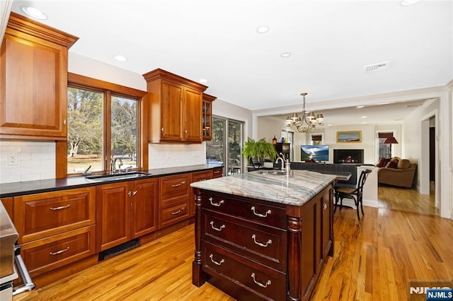 kitchen with a kitchen island with sink, a sink, visible vents, open floor plan, and dark stone counters