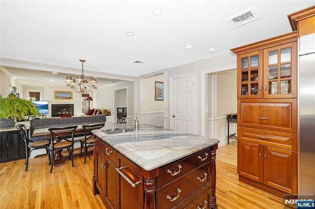 kitchen with visible vents, glass insert cabinets, open floor plan, a sink, and light stone countertops