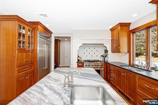 kitchen featuring premium appliances, visible vents, glass insert cabinets, a sink, and dark stone countertops