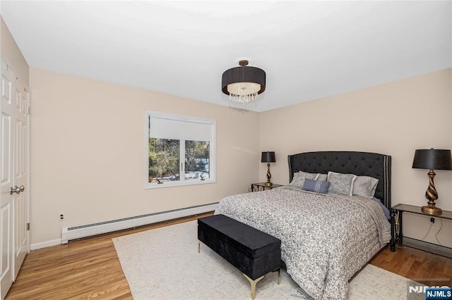 bedroom with a baseboard heating unit, light wood finished floors, and baseboards