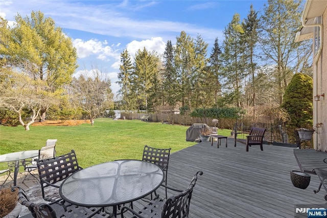 deck featuring outdoor dining area, fence, and a lawn