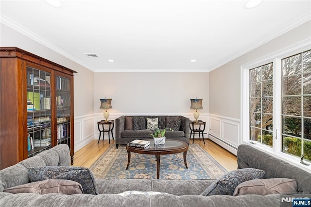 living room with a baseboard radiator, light wood-style flooring, a wainscoted wall, visible vents, and crown molding