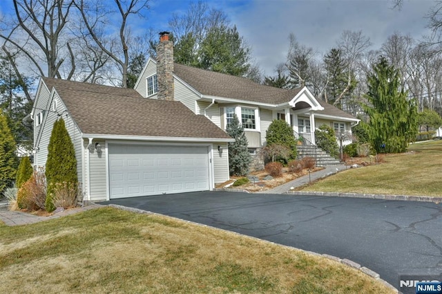 view of front of house featuring a front lawn, aphalt driveway, a shingled roof, a garage, and a chimney