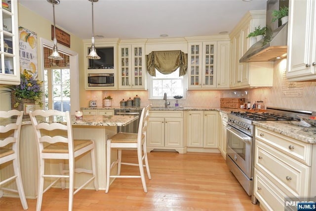 kitchen featuring cream cabinetry, appliances with stainless steel finishes, wall chimney exhaust hood, and a breakfast bar