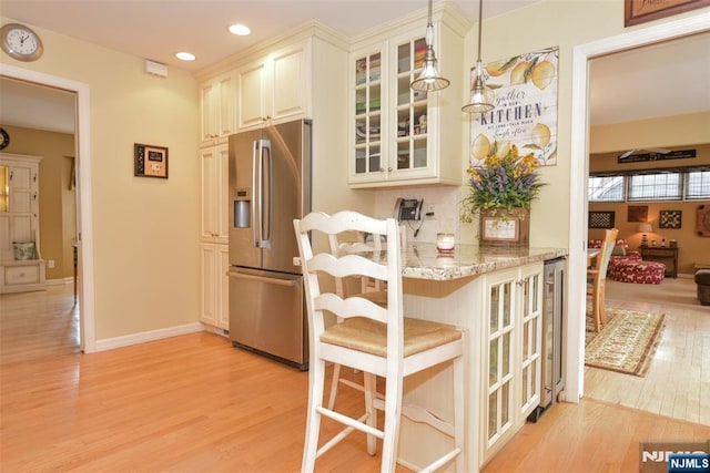 kitchen with light wood-style flooring, glass insert cabinets, stainless steel fridge, and light stone countertops