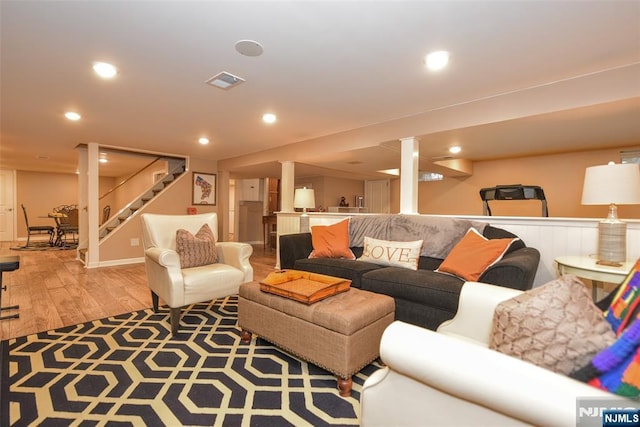 living area with light wood-style flooring, visible vents, recessed lighting, and stairs