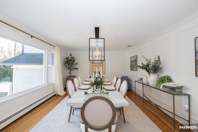 dining room featuring a baseboard radiator, ornamental molding, a decorative wall, and wood finished floors