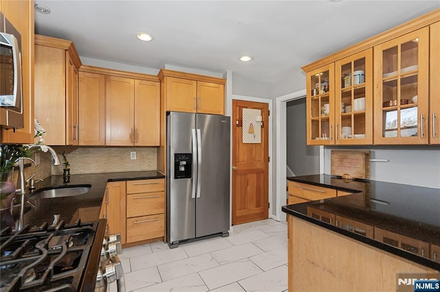 kitchen featuring decorative backsplash, stainless steel appliances, dark stone counters, and sink