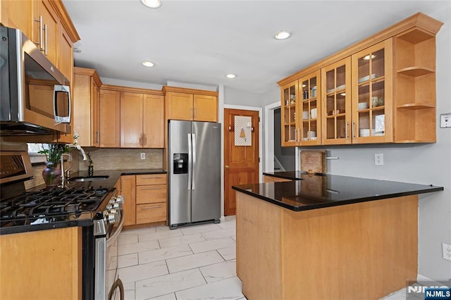 kitchen featuring dark stone countertops, appliances with stainless steel finishes, sink, backsplash, and kitchen peninsula