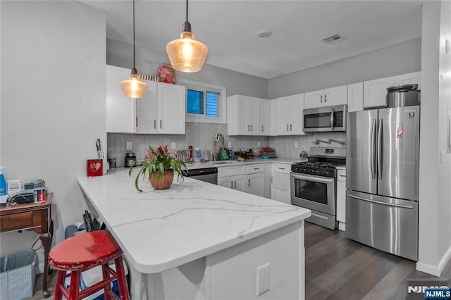 kitchen featuring kitchen peninsula, appliances with stainless steel finishes, white cabinets, and a breakfast bar