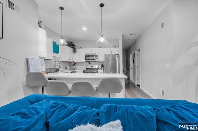 kitchen with white cabinetry, kitchen peninsula, stainless steel appliances, decorative light fixtures, and a kitchen bar