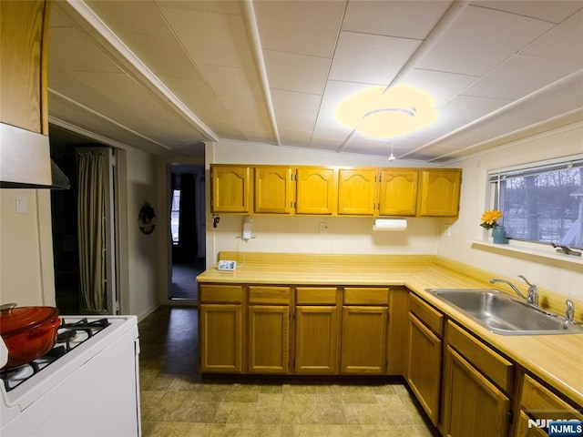 kitchen featuring brown cabinets, light countertops, a sink, and white gas stove