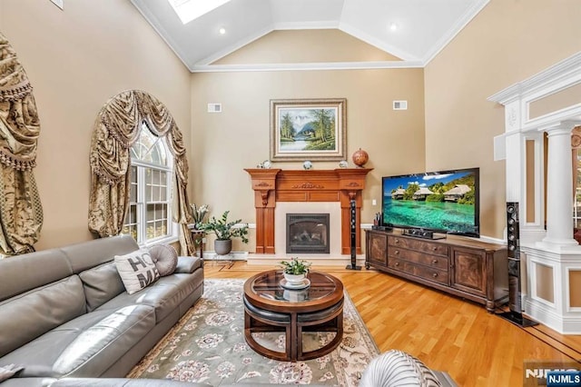 living room with wood-type flooring, decorative columns, a skylight, high vaulted ceiling, and ornamental molding