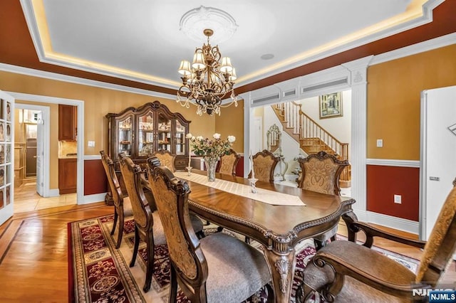 dining space featuring light hardwood / wood-style floors, a tray ceiling, a notable chandelier, and ornamental molding