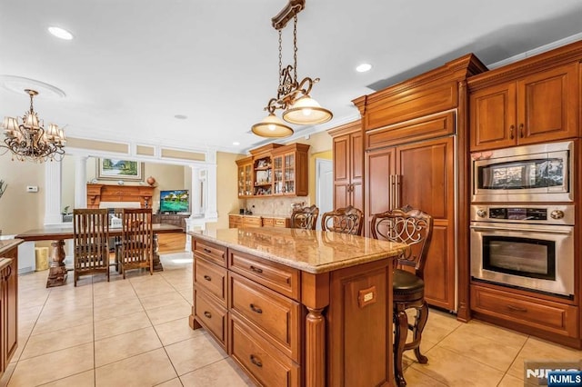 kitchen featuring a kitchen bar, a center island, pendant lighting, stainless steel appliances, and ornate columns