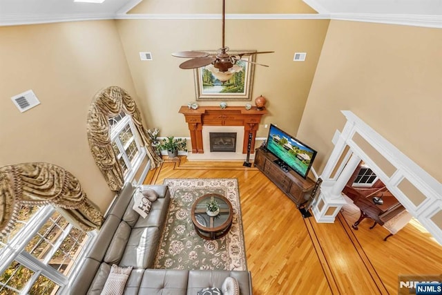 living room with a high ceiling, ornamental molding, hardwood / wood-style floors, and ceiling fan