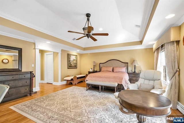 bedroom with hardwood / wood-style floors, ceiling fan, a baseboard radiator, a raised ceiling, and ornamental molding