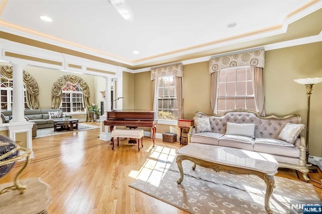 living area featuring light wood-type flooring, ornate columns, ornamental molding, and a tray ceiling