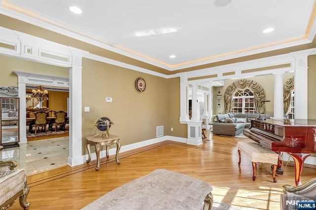 living area featuring decorative columns, ornamental molding, a chandelier, and wood-type flooring