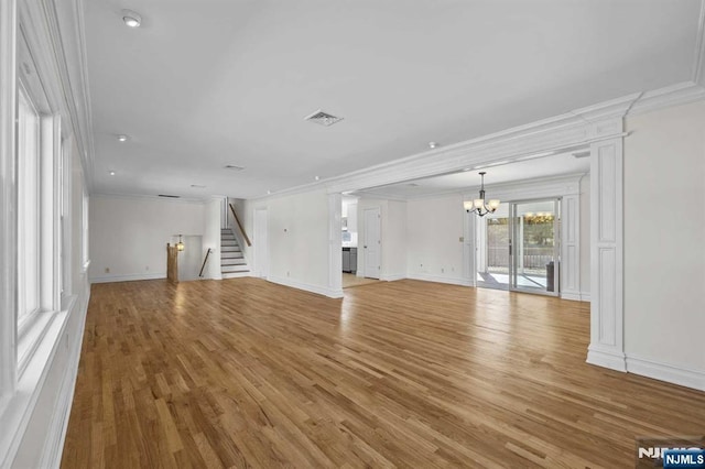 unfurnished living room with crown molding, light wood finished floors, visible vents, stairway, and an inviting chandelier