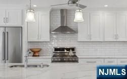 kitchen featuring white cabinets, stainless steel appliances, wall chimney exhaust hood, and decorative backsplash