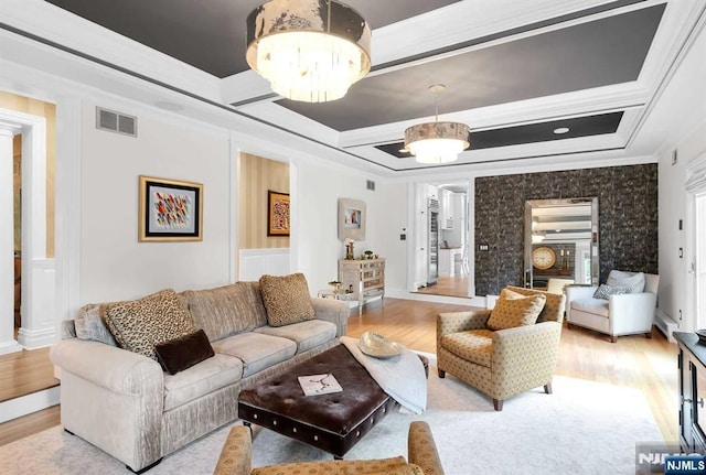 living room featuring decorative columns, visible vents, light wood-style flooring, ornamental molding, and an inviting chandelier