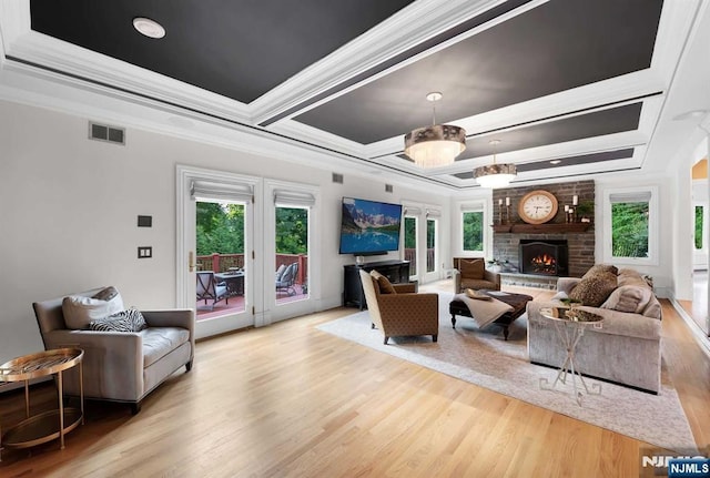 living room with a large fireplace, light wood-type flooring, a raised ceiling, and visible vents