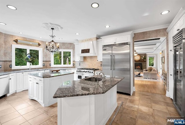 kitchen featuring a center island, pendant lighting, high end appliances, a sink, and dark stone counters