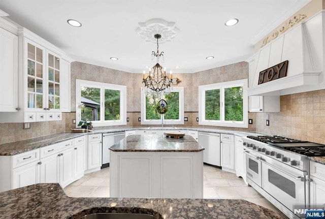 kitchen with a kitchen island, appliances with stainless steel finishes, dark stone countertops, glass insert cabinets, and pendant lighting