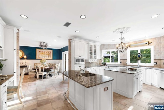 kitchen featuring a center island with sink, stainless steel appliances, hanging light fixtures, glass insert cabinets, and a chandelier