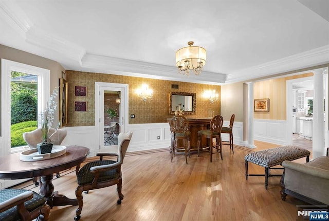 dining space featuring a chandelier, wainscoting, light wood-type flooring, and ornate columns