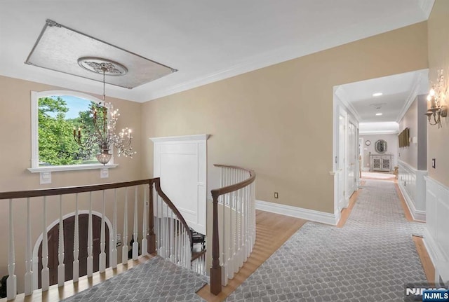 hall featuring crown molding, a notable chandelier, light wood-style flooring, wainscoting, and an upstairs landing