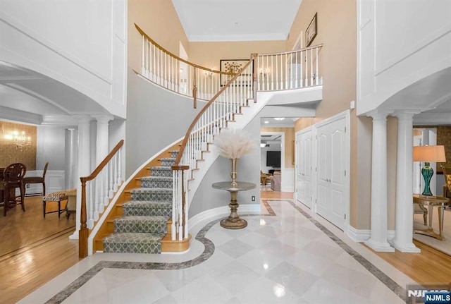 stairs featuring crown molding, decorative columns, a towering ceiling, and baseboards