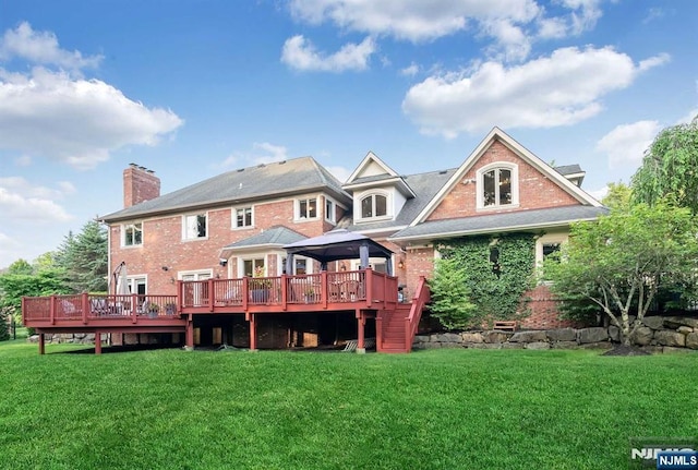 back of house featuring a wooden deck, a chimney, a gazebo, a yard, and brick siding