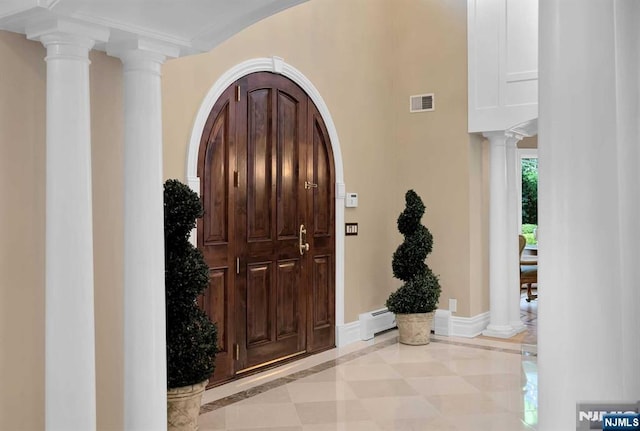 entrance foyer featuring baseboards, visible vents, arched walkways, ornate columns, and a baseboard heating unit