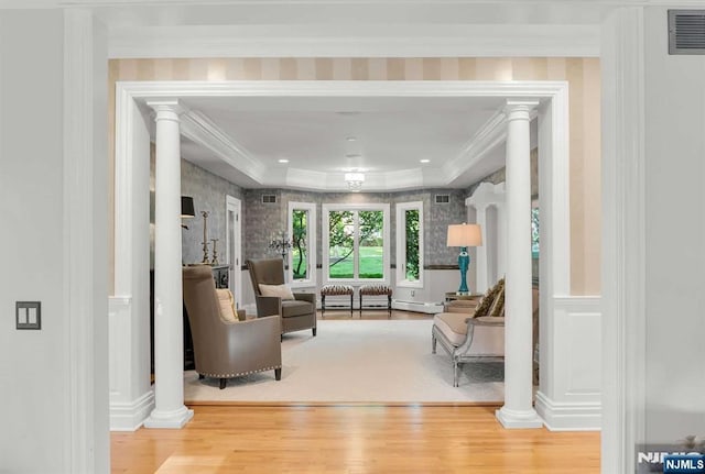 living area with crown molding, wood finished floors, visible vents, and ornate columns