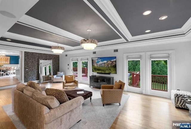 living area with ornamental molding, french doors, light wood-type flooring, and a raised ceiling