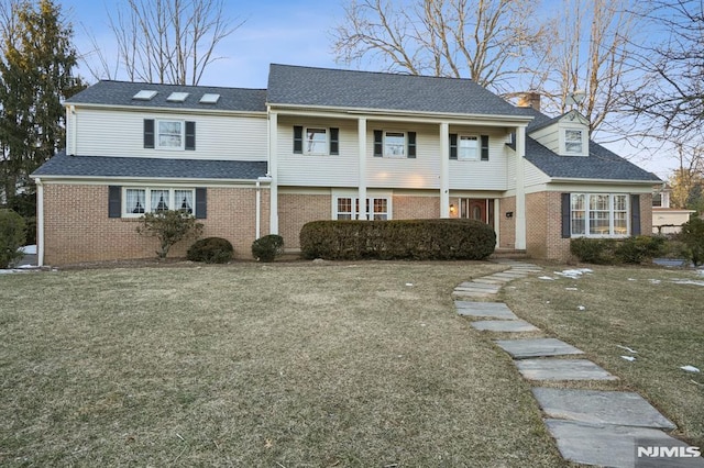 view of front facade with a front yard, brick siding, a chimney, and roof with shingles