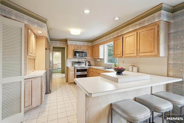 kitchen featuring stainless steel appliances, a peninsula, a sink, light countertops, and a kitchen bar