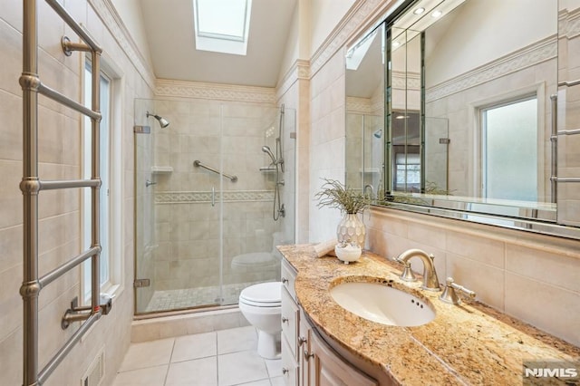 bathroom featuring a skylight, toilet, vanity, a shower stall, and tile walls