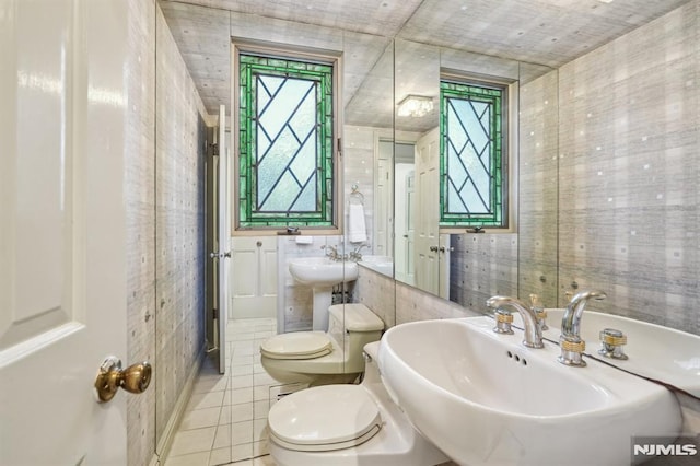 bathroom with toilet, a sink, tile walls, and tile patterned floors