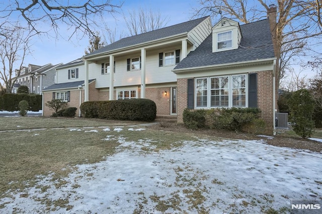 view of front of home with roof with shingles, a chimney, central AC unit, and brick siding