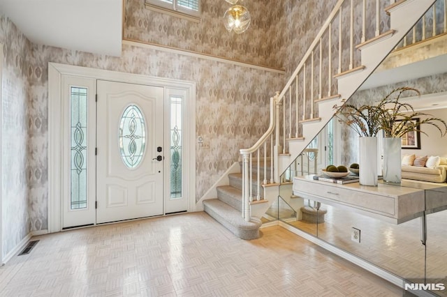 entryway with visible vents, stairway, a high ceiling, baseboards, and wallpapered walls